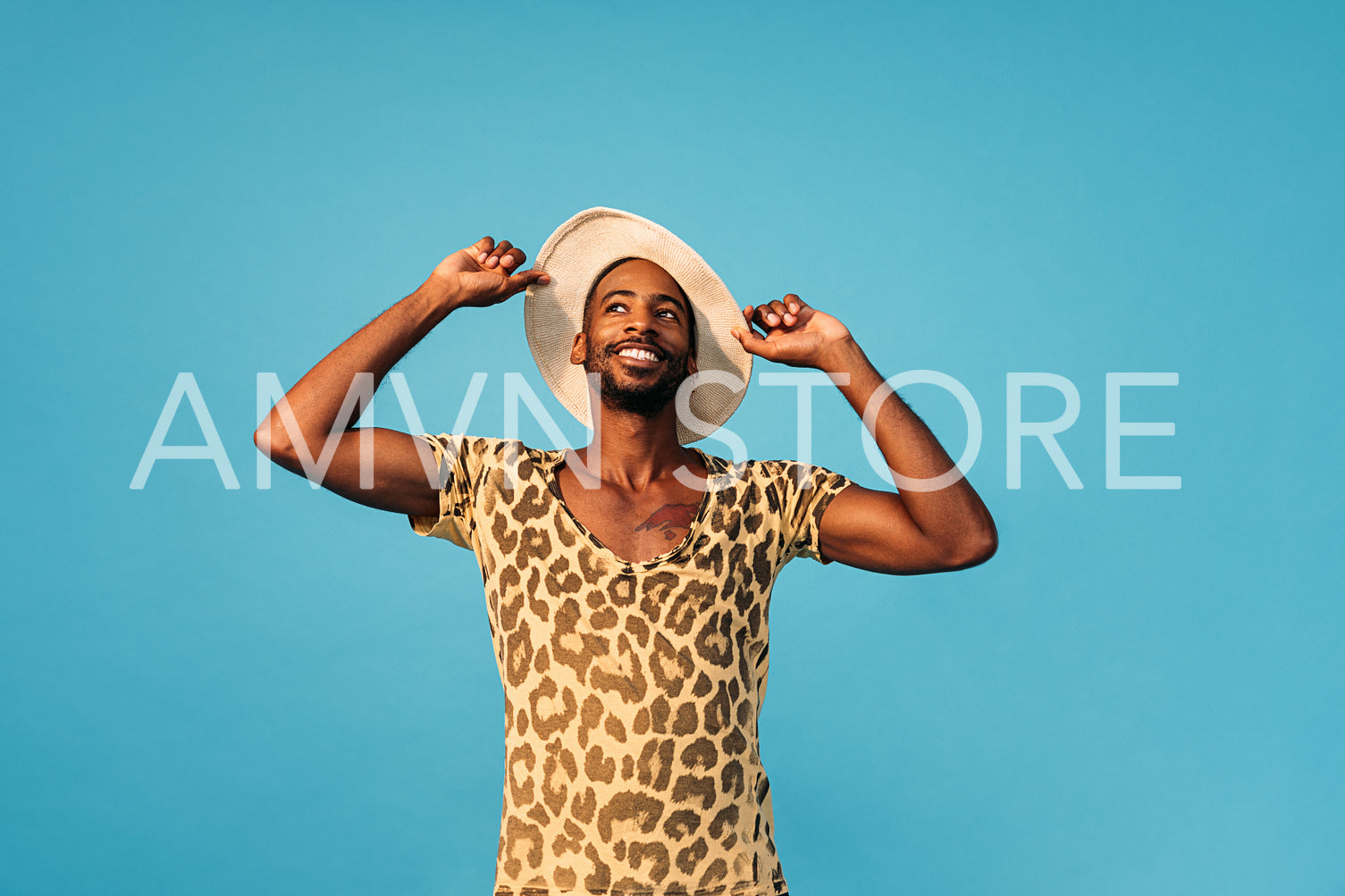 Smiling stylish man holding his straw hat and looking up against the blue background