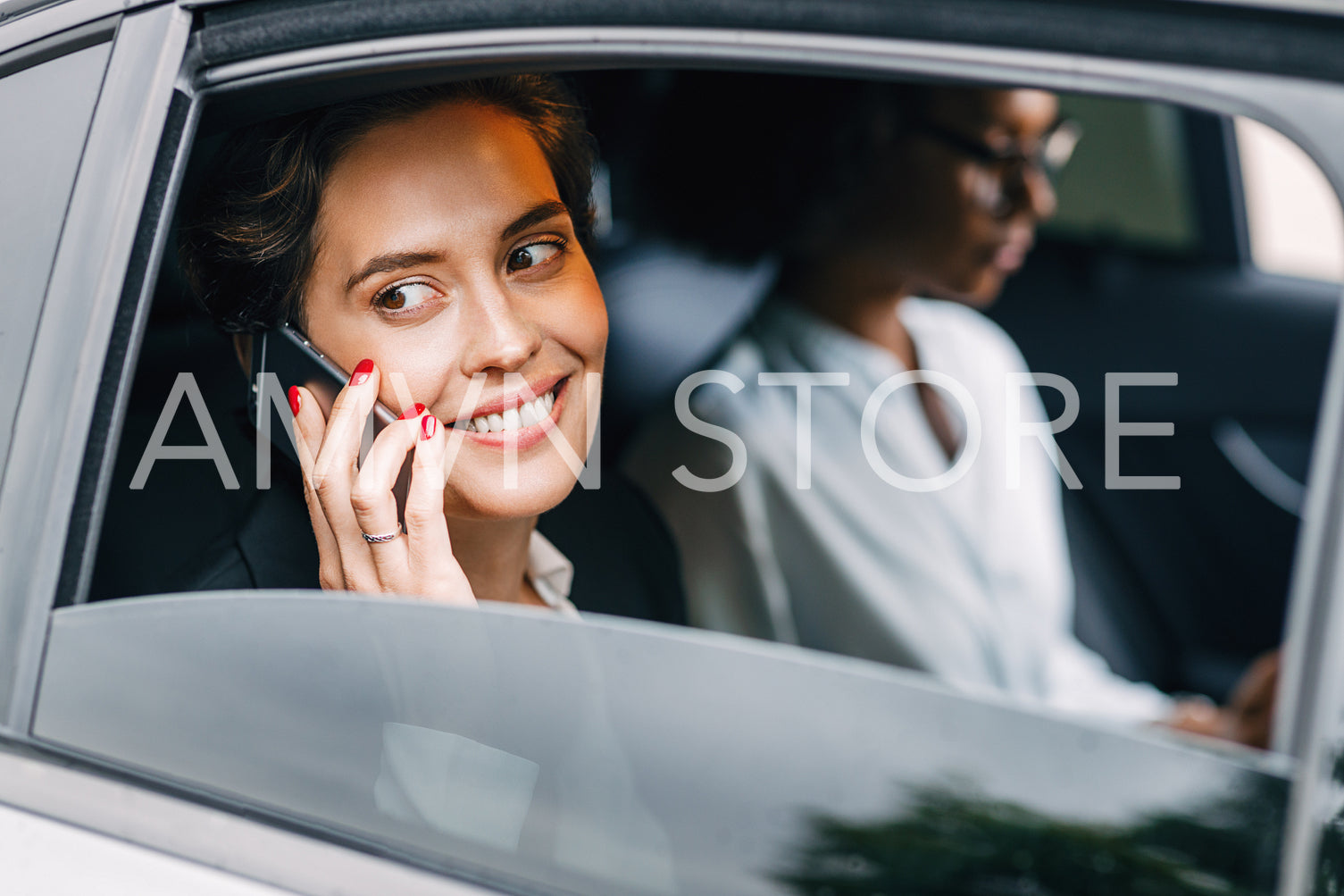 Smiling woman talking on a cell phone in a taxi. Young entrepreneur sitting on a backseat with a colleague.	