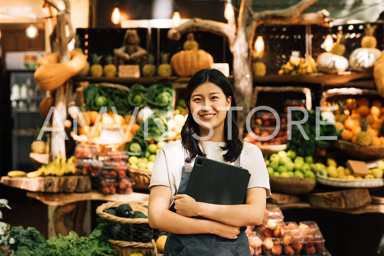 Smiling entrepreneur holding a digital tablet standing at an outdoor market. Asian woman in an apron looking at camera while standing against a street food market.