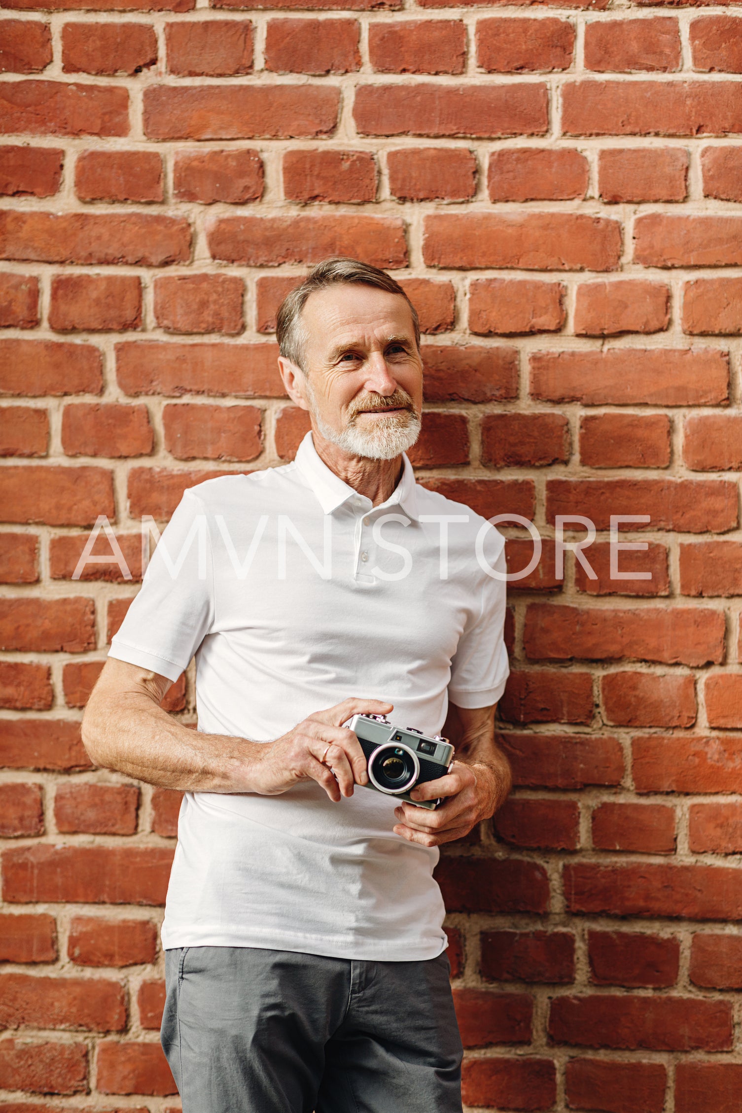 Senior man standing with a film camera outdoors at a brick wall	