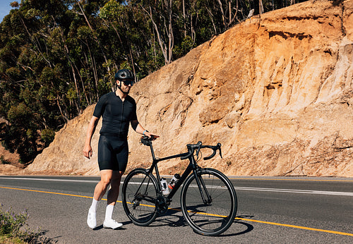 Young male cyclist holding his bicycle by a saddle walking on an empty road