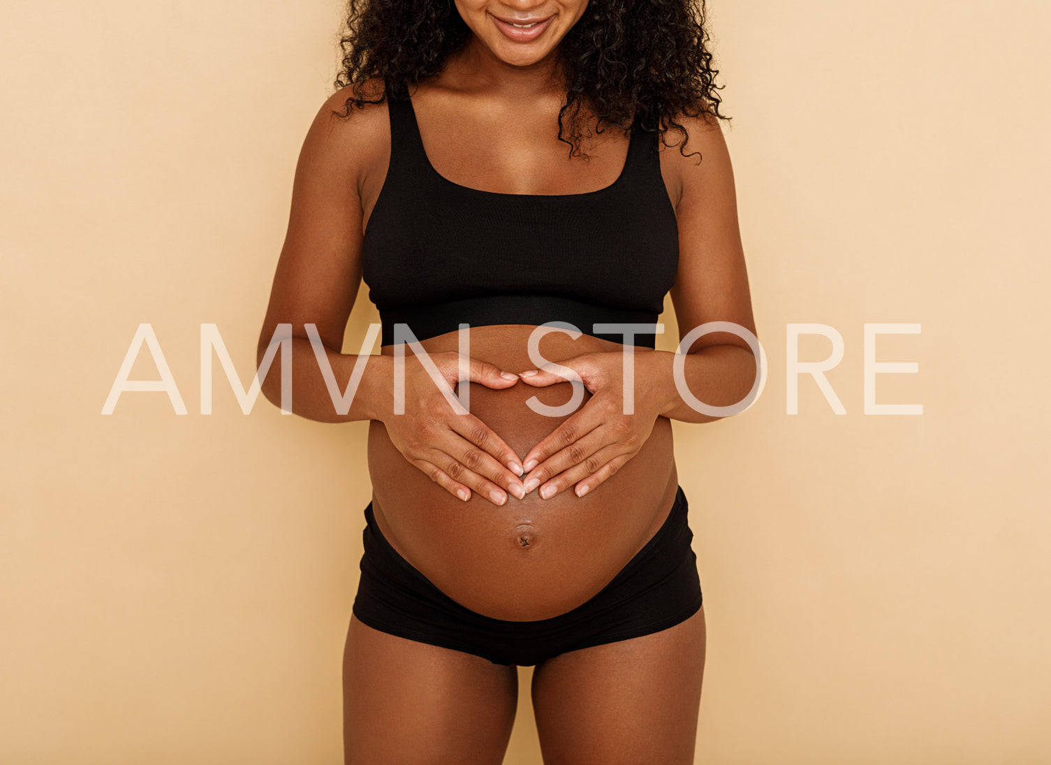 Studio shot of a pregnant woman making a heart shaped gesture over her belly	