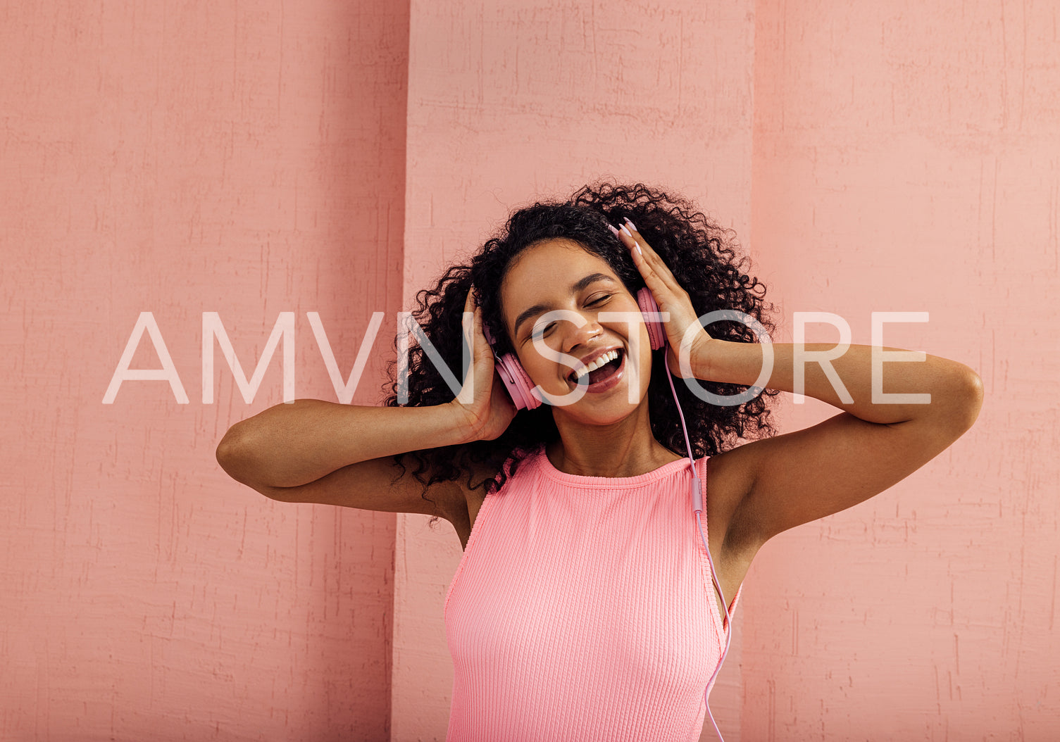 Portrait of a young laughing woman wearing pink headphones standing with closed eyes