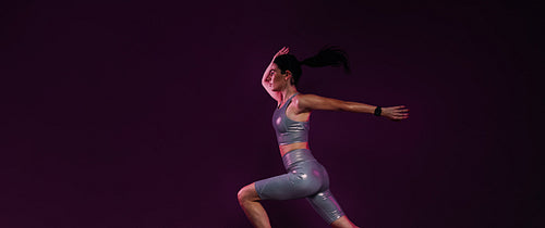 Side view of young female sprinting over a magenta backdrop