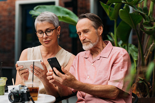 Mature couple using their smartphones while sitting together in an outdoor cafe