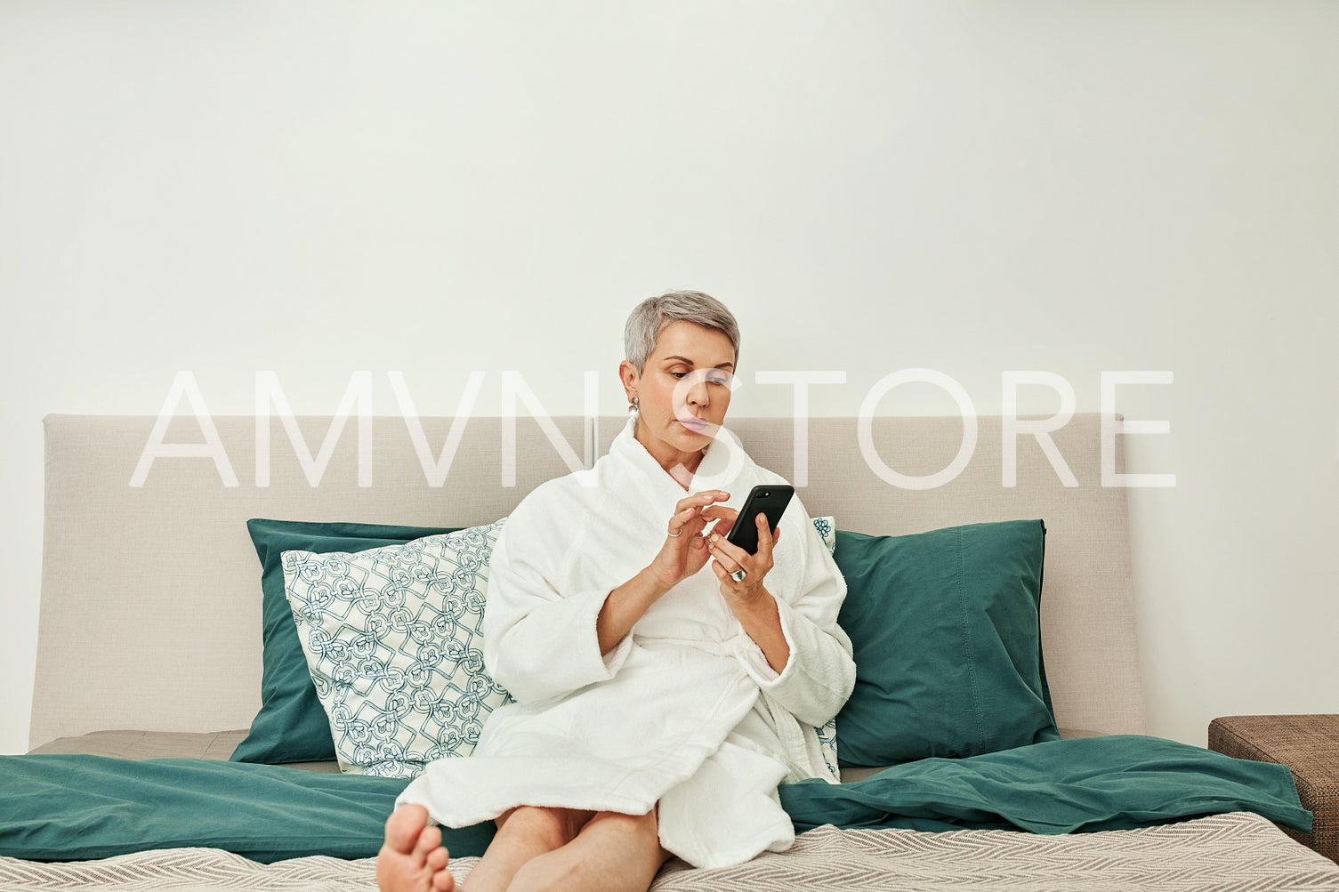 Senior woman typing on her smartphone lying on a bed