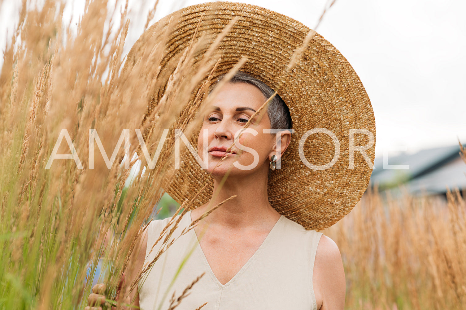 Senior female with short grey hair wearing a straw hat looking at wheat