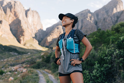 Laughing woman in sportswear standing against mountains. Young smiling female relaxing during hike.