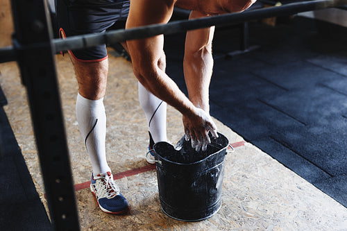 Young unrecognizable muscular man preparing hands with chalk powder, for barbell training in gym