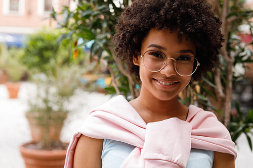 Outdoor portrait of a beautiful girl wearing glasses, looking at a camera and smiling