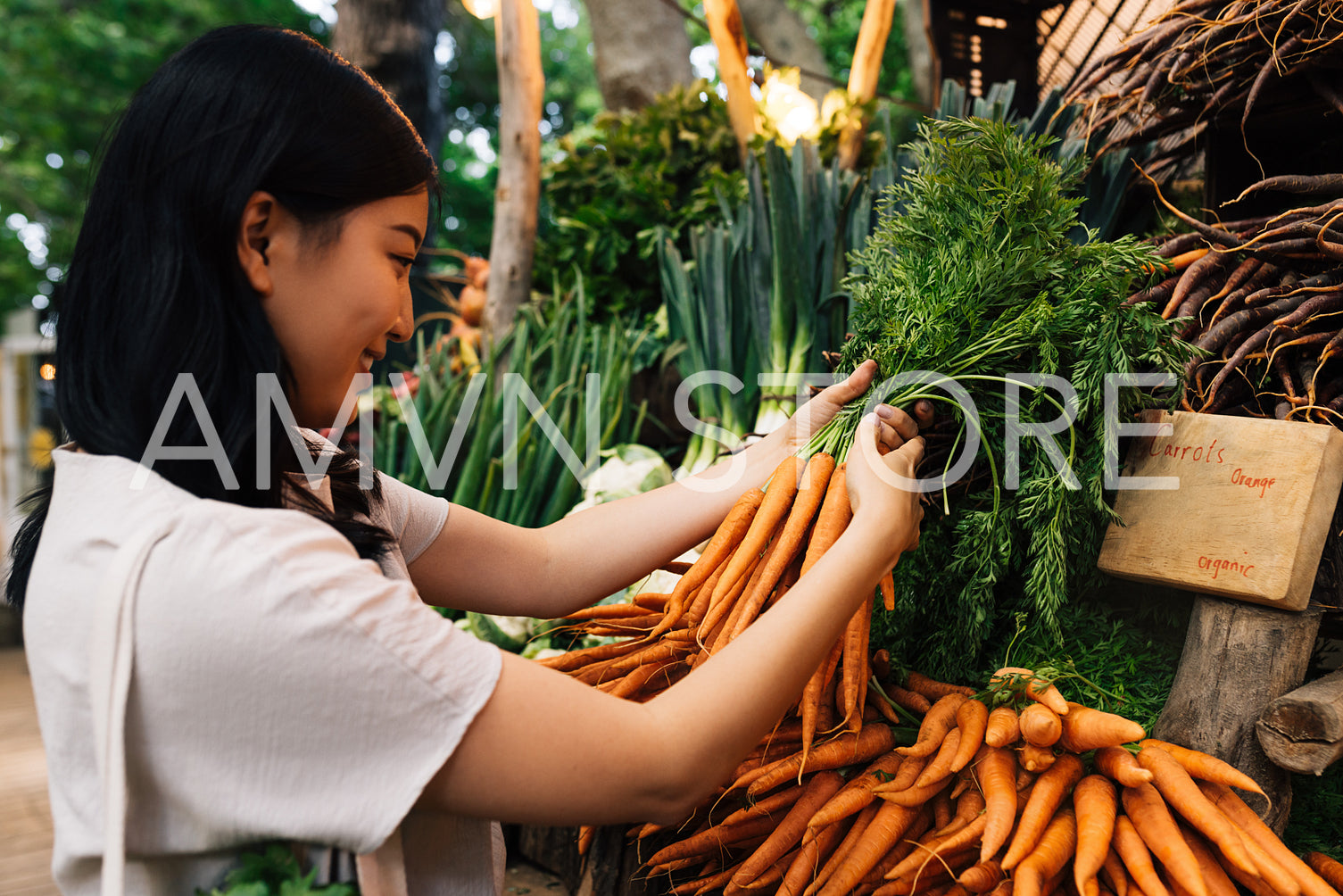 Woman buying carrot on the farmers market. Young female holding a bunch of carrots.