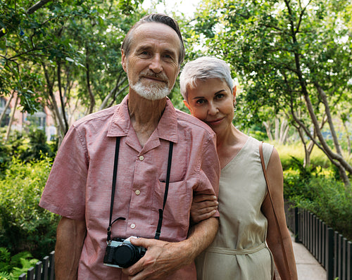 Portrait of two aged people looking at a camera in the park. Mature husband and his wife looking at the camera.