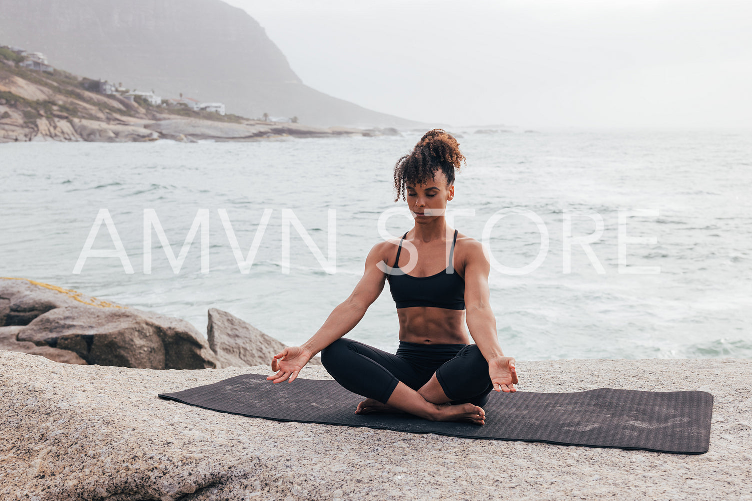 Woman meditating on mat. Female with crossed legs practicing yoga by ocean.