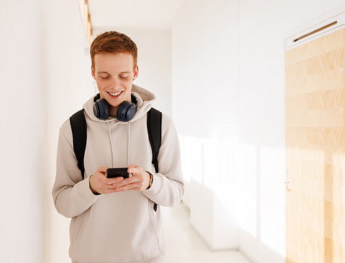 Smiling guy using smartphone while walking in college corridor