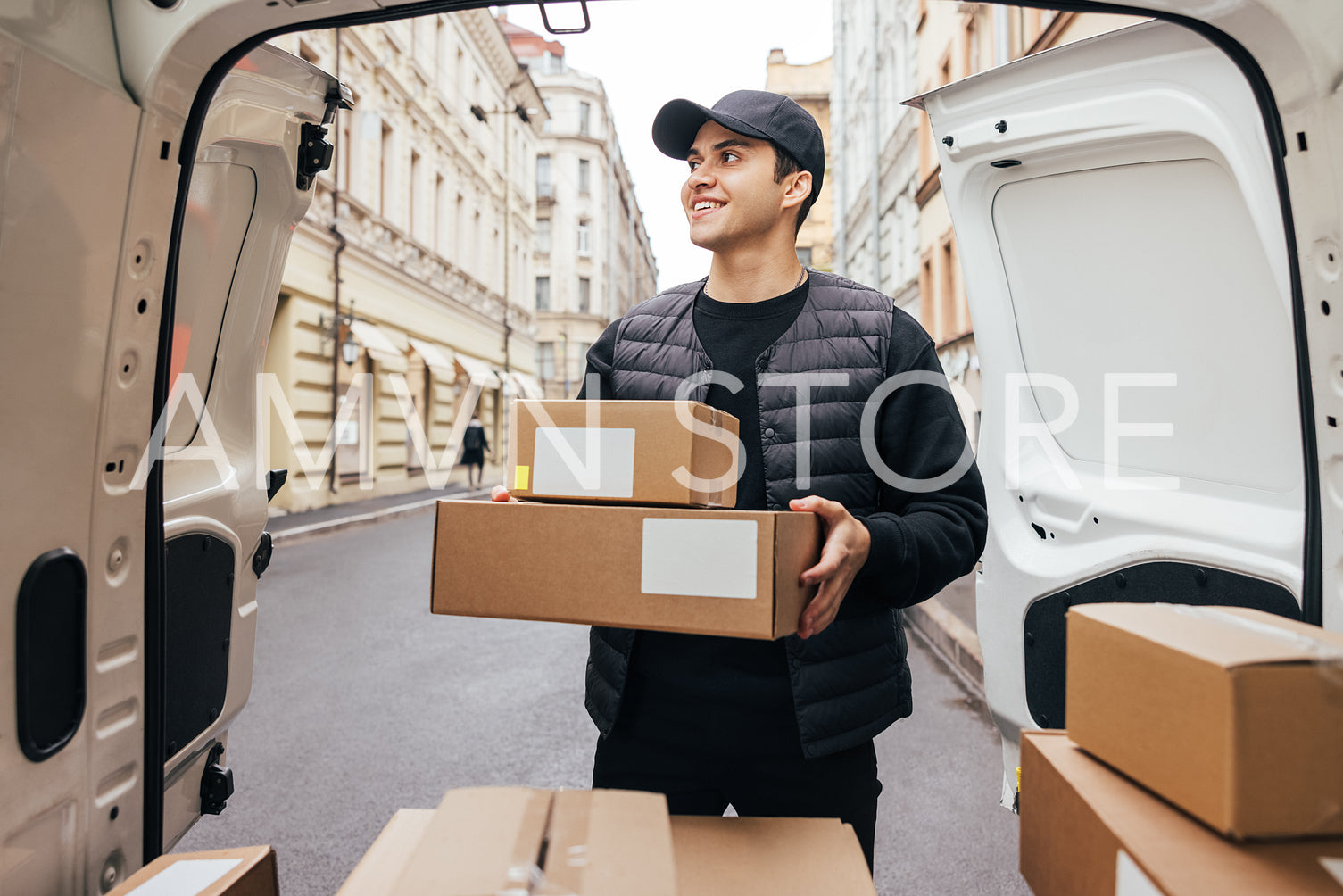 Male courier in uniform standing at van trunk holding boxes prep