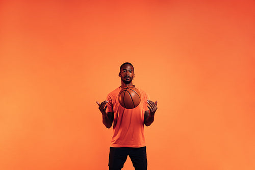 Serious guy in sportswear throws a basketball in front of him in the studio