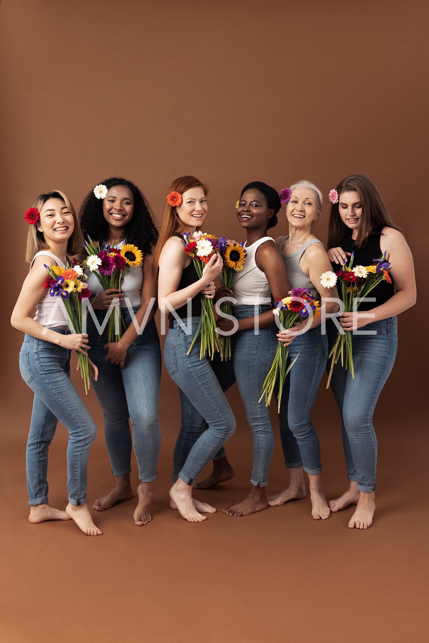 Full body shot of six women of different ages standing together with bouquets of flowers. Smiling women in casuals with flowers in hair.