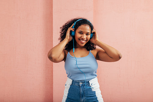 Smiling woman in casual clothes wearing blue headphones and looking at camera