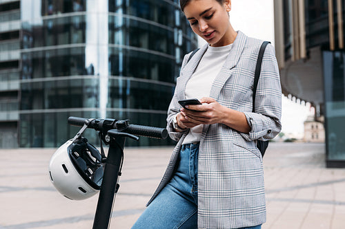 Woman using an app to unlock the electric push scooter. Businesswoman holding smartphone while standing in the city.