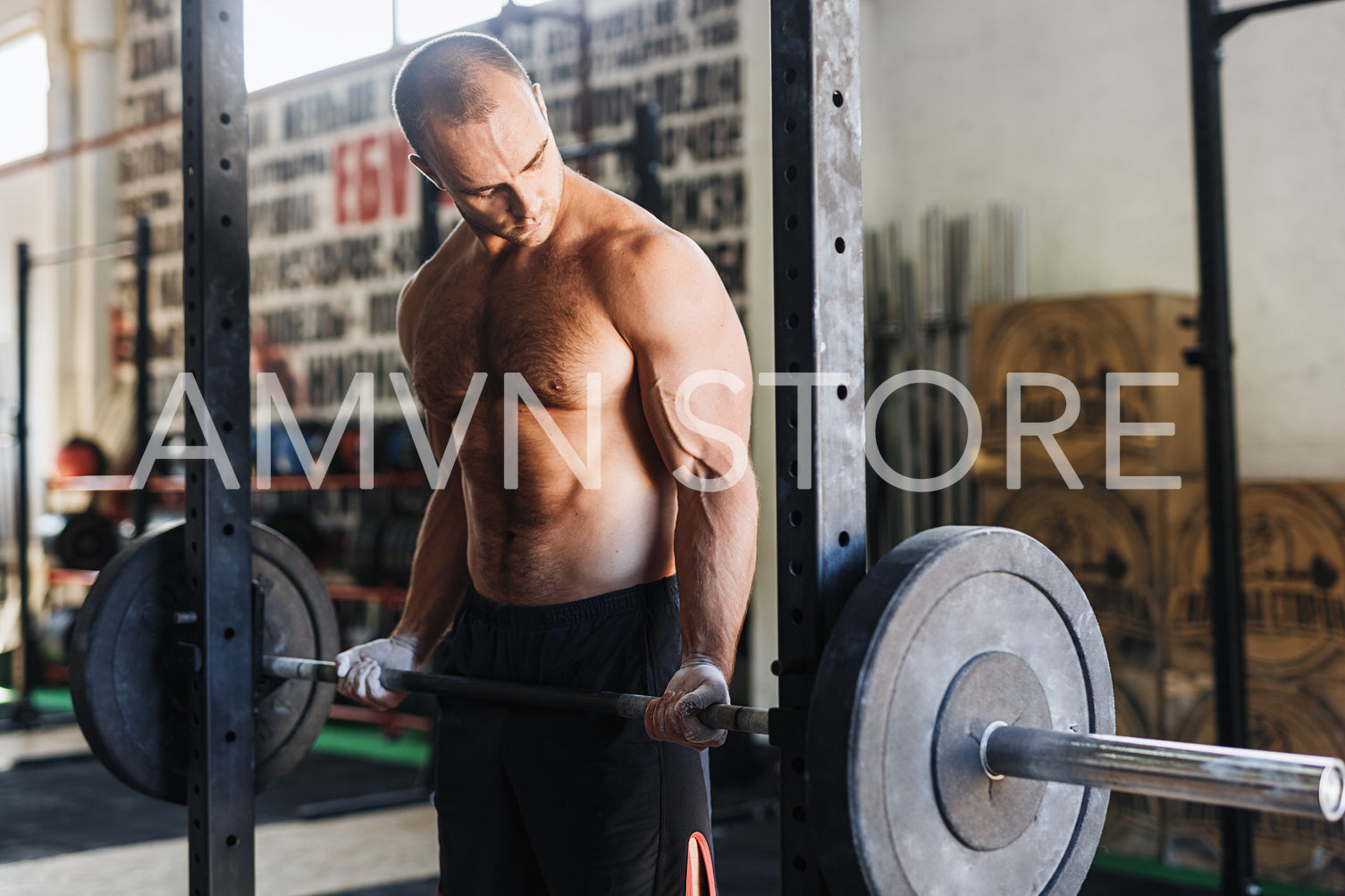 Side view of male athlete looking at his muscles while lifting barbell in gym	