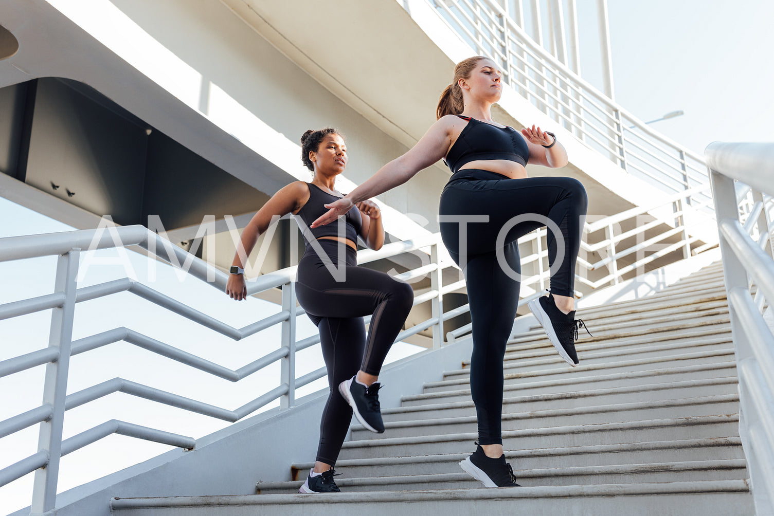 Full length of two plus size females going warm up on staircase synchronously. Female friends exercising together in the city.