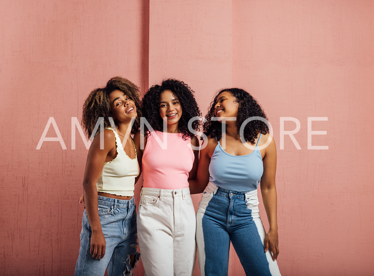 Female friends with curly hair posing together against pink wall