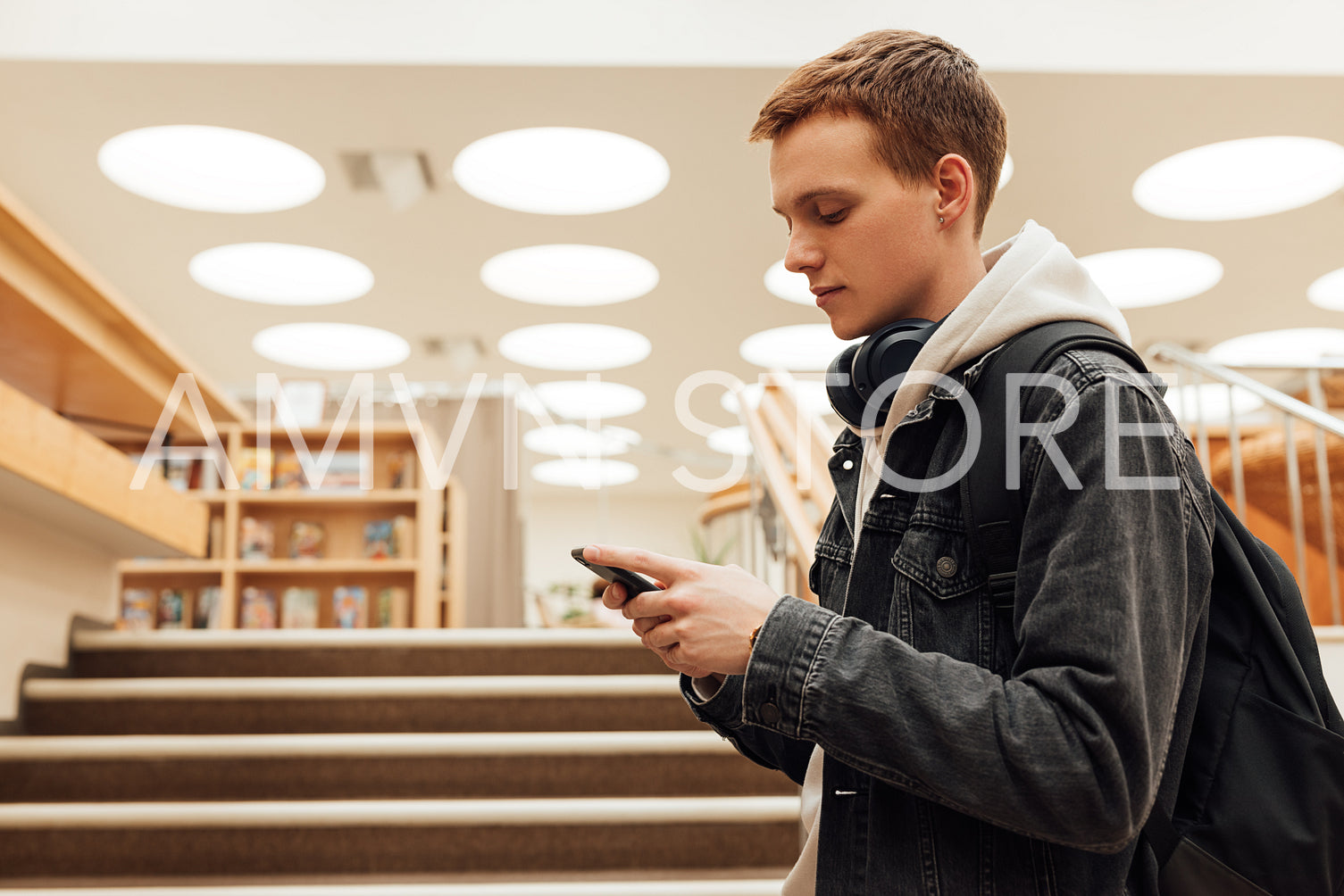 Young male with backpack and smartphone standing in library