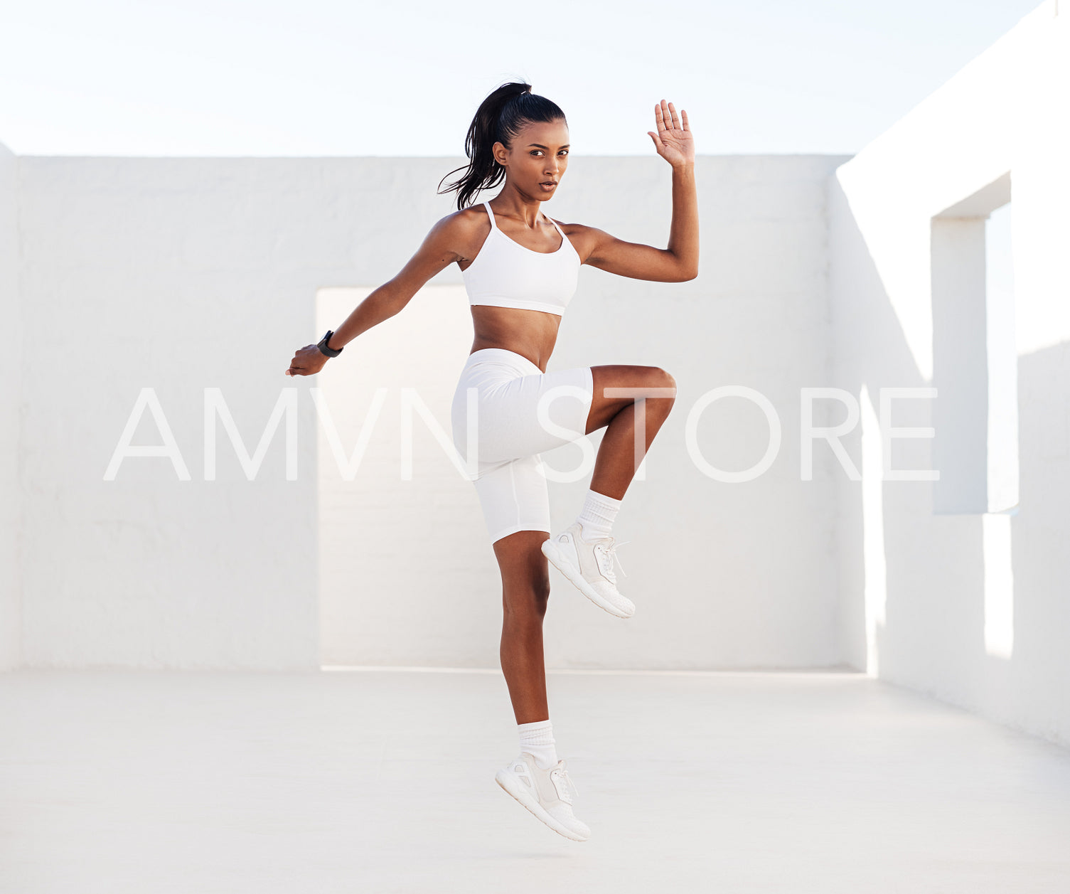 Slim female jumping in the white outdoor studio doing cardio exercises. Side view of a professional fitness athlete practicing outdoors.