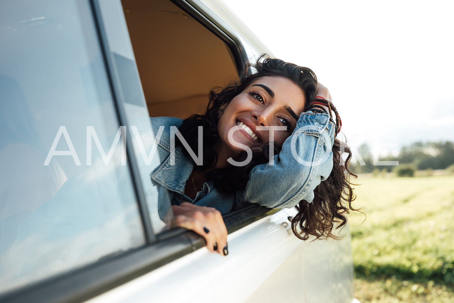 Attractive young woman enjoying road trip. Smiling female looks out of van window.