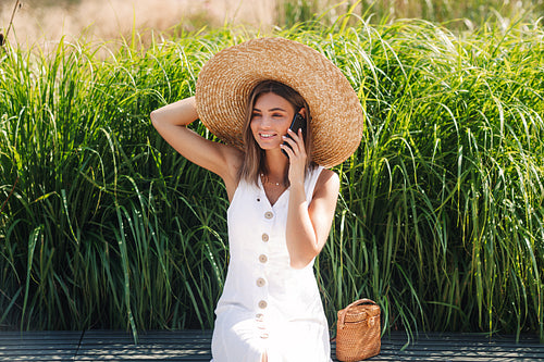 Smiling woman wearing big hat talking on cell phone in the park