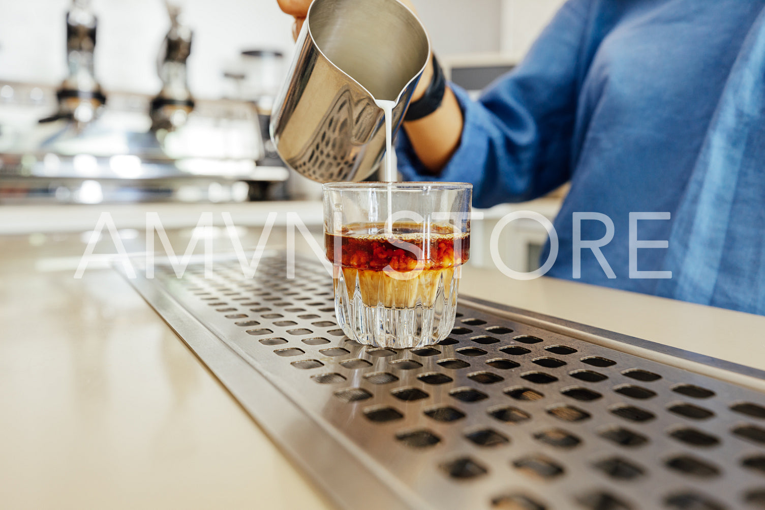 Unrecognizable barista pouring milk from a stainless steel milk jug into a glass for flat white	