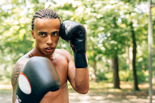 Young kickboxer with guard mouth and gloves practicing punches outdoors