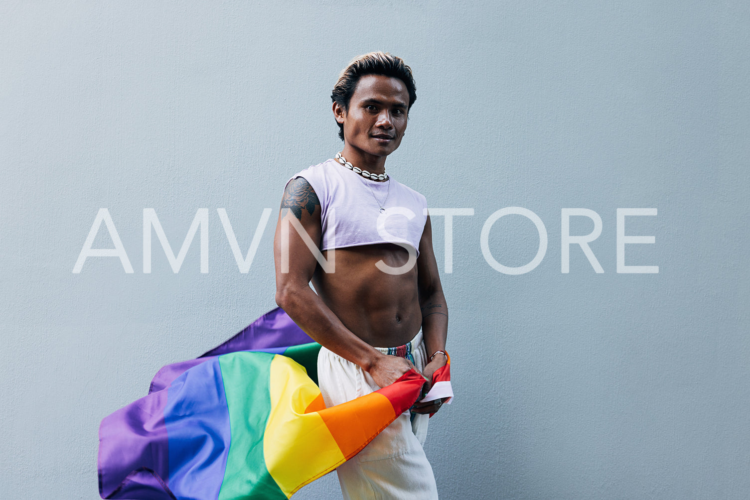 Young guy with LGBT flag posing at grey wall outdoors