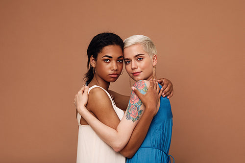 Two beautiful women embracing in the studio. Females in dresses looking at camera