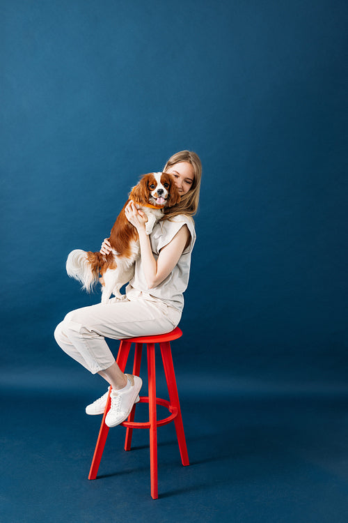 Young pet owner sitting on a red chair in studio holding a littl