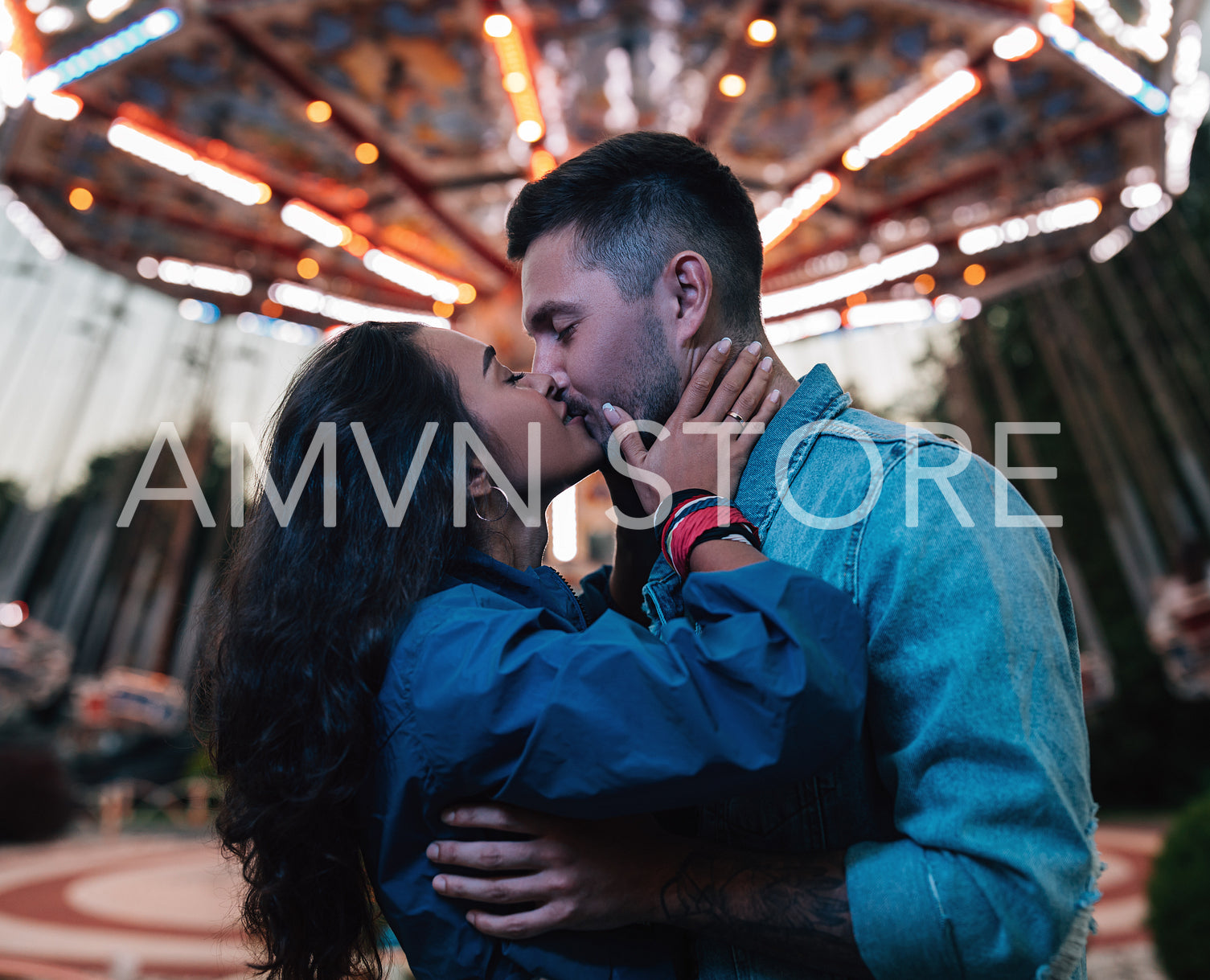 Young couple kissing against carousel. Male and female hugging and kissing in the evening in an amusement park.