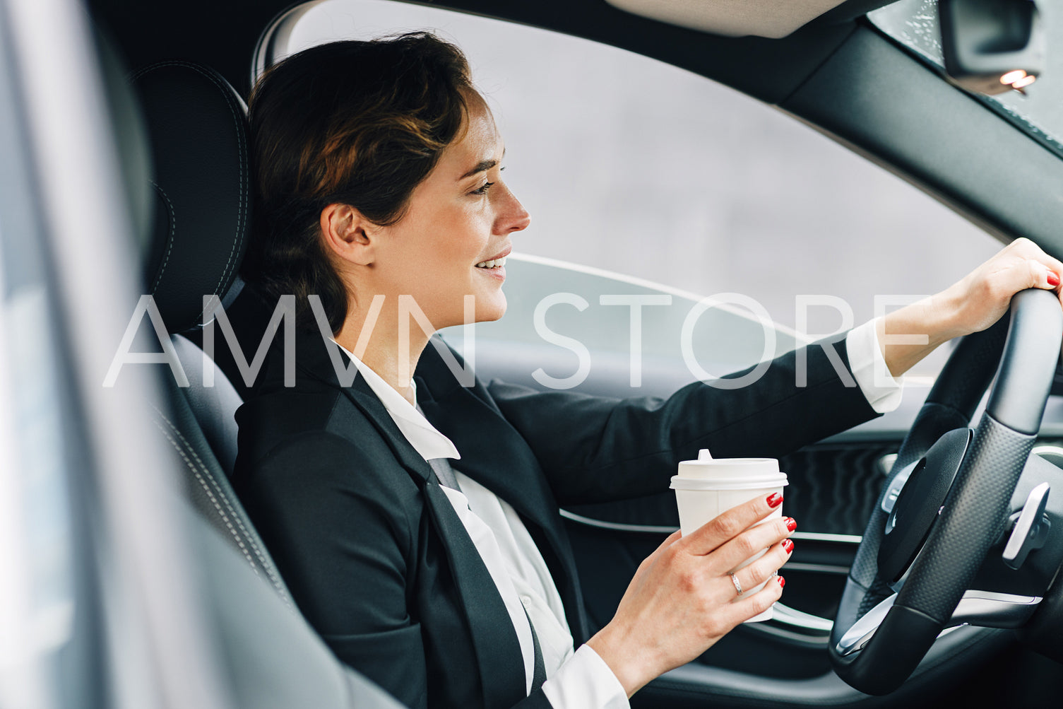 Side view of a smiling businesswoman holding a coffee and driving a car	