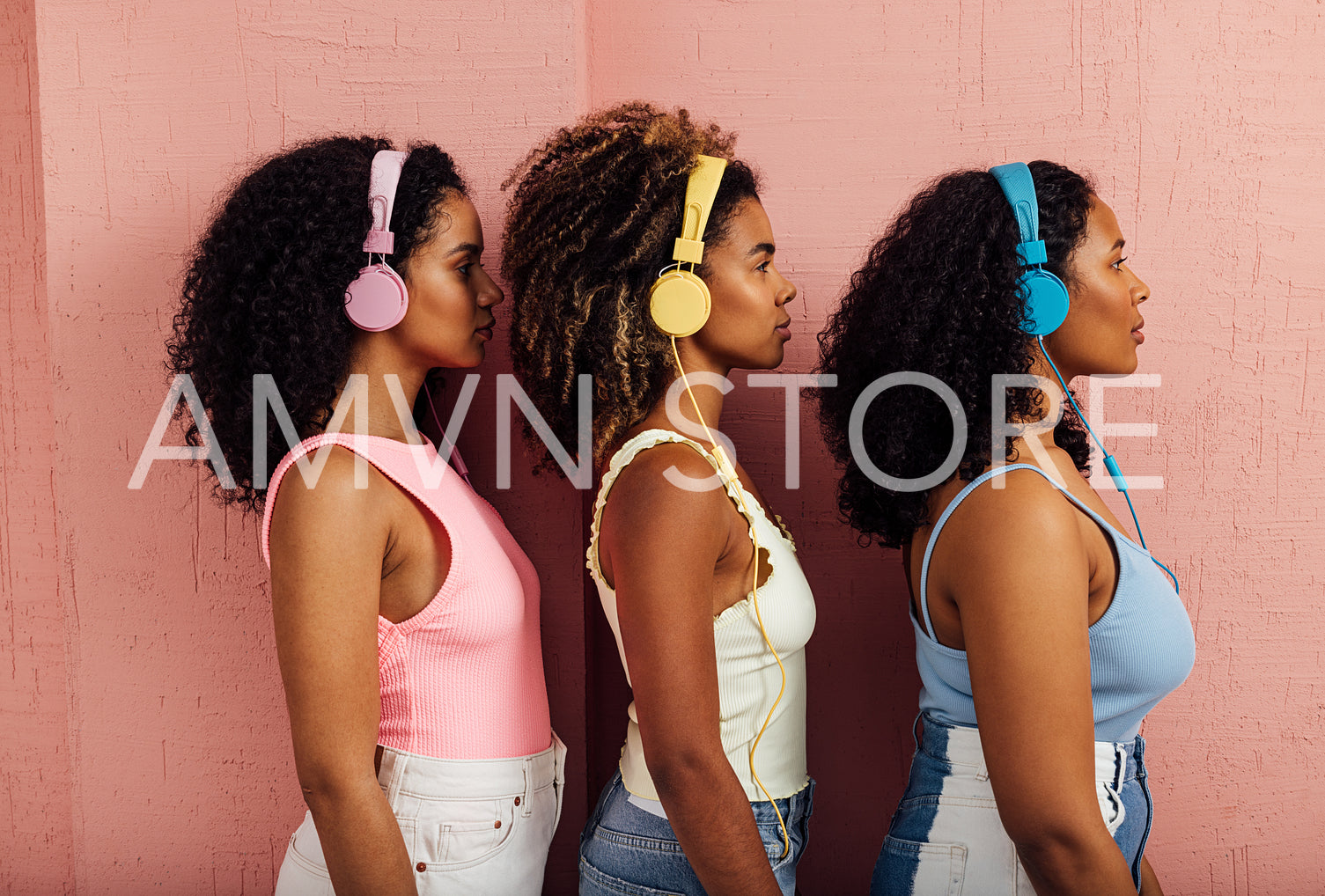 Side view of three women wearing headphones standing one after another against a pink wall