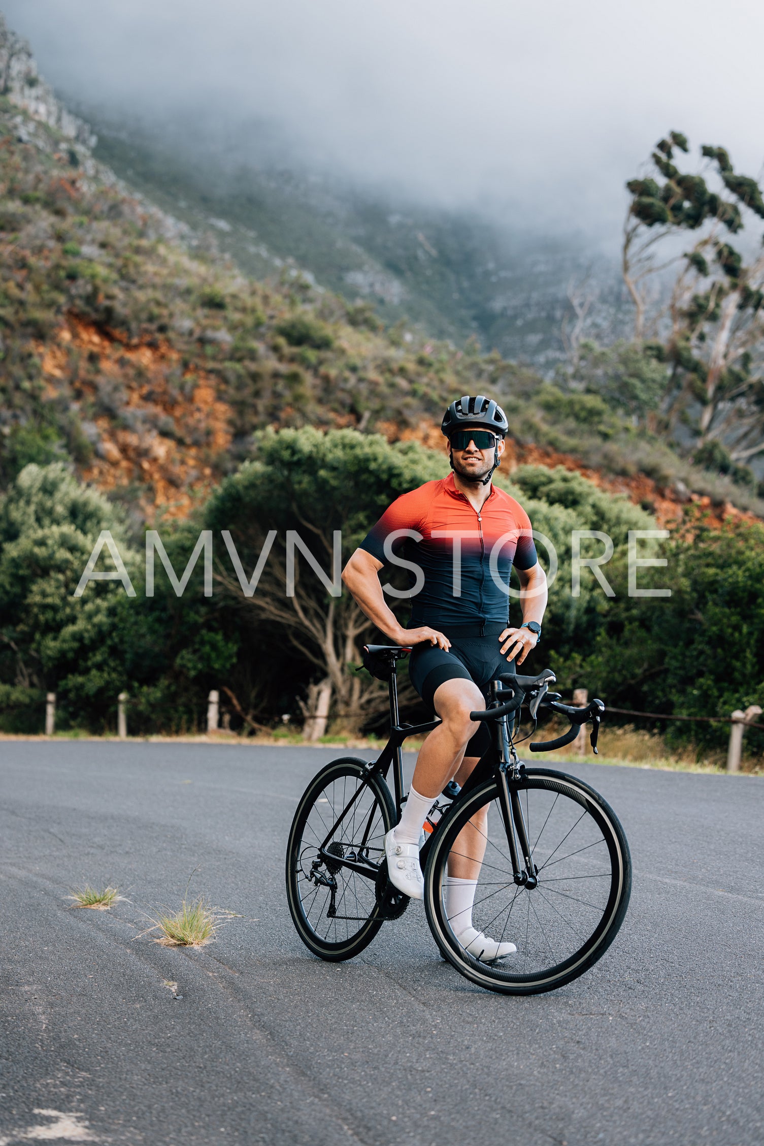 Male cyclist in sports clothes standing with a road bike against a mountain with clouds