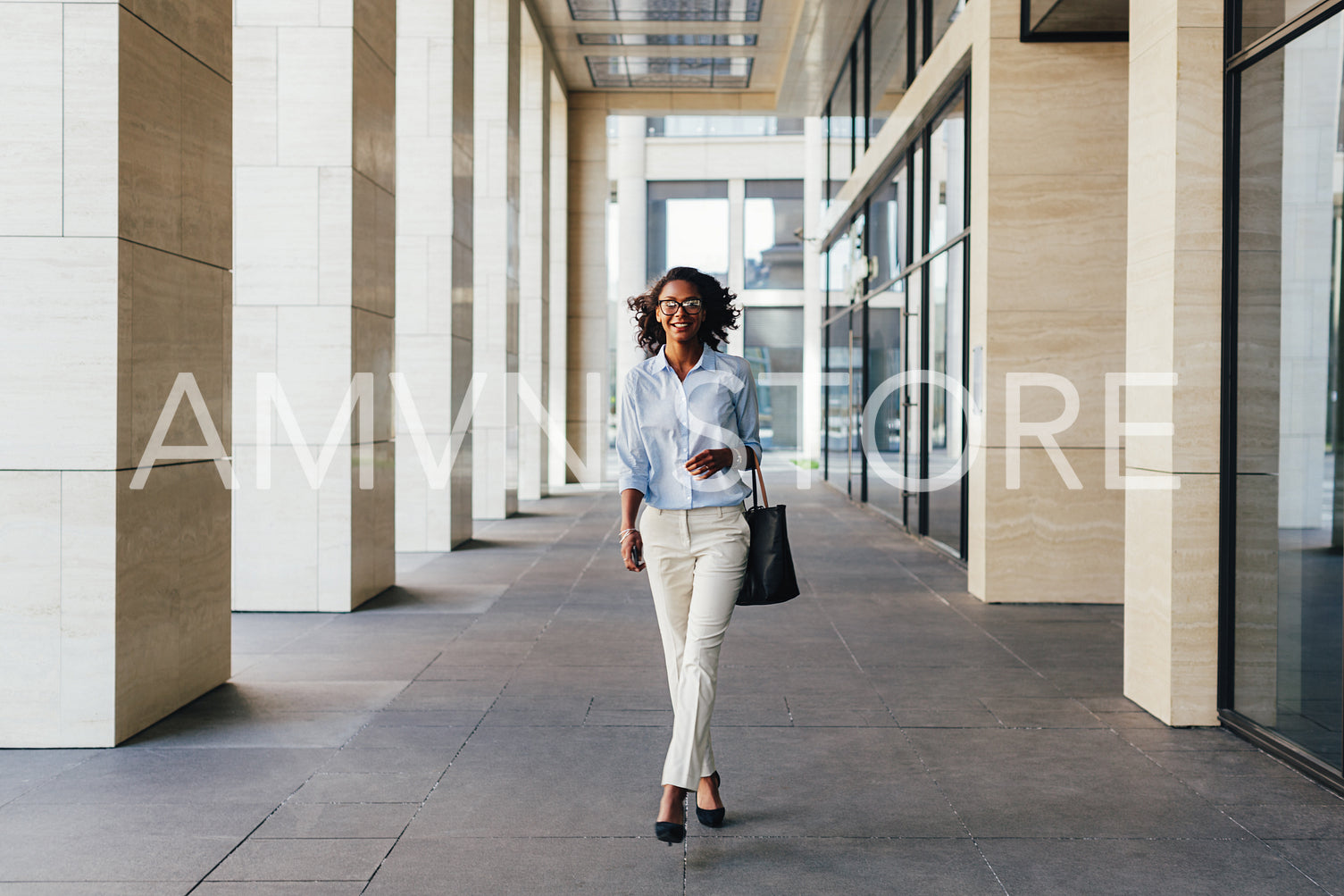 Young smiling woman walking on city street to office carrying her bag	