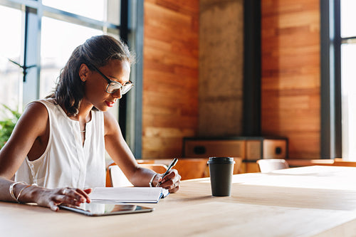 Beautiful young woman sitting in the cafe writing notes in her diary. Business person working indoors.