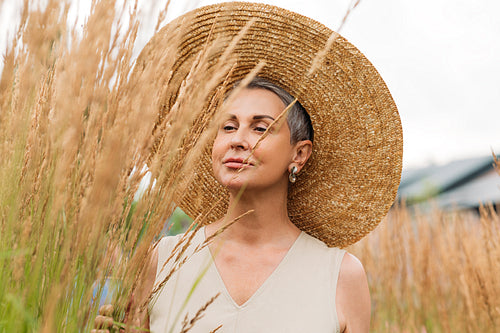 Senior female with short grey hair wearing a straw hat looking at wheat