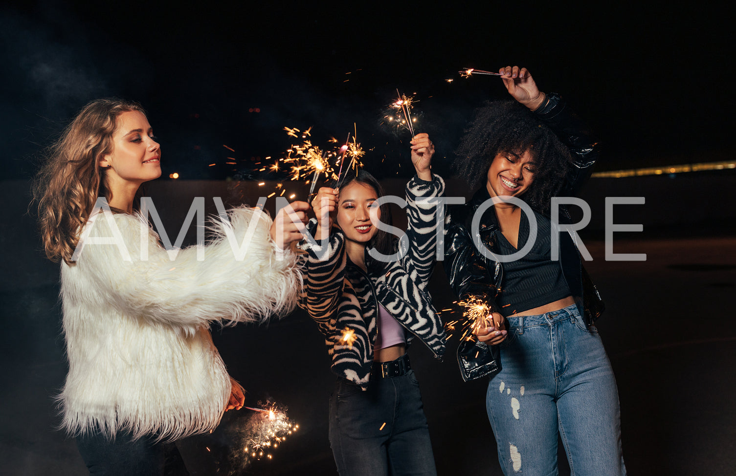 Three girls walking at night with sparklers. Young stylish women enjoying party outdoors.	