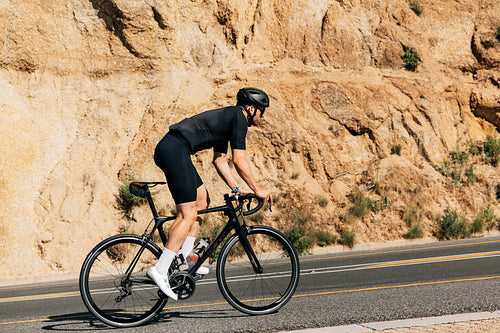 Cyclist in black sportswear doing intense training outdoors. Side view of a triathlete on a bicycle.