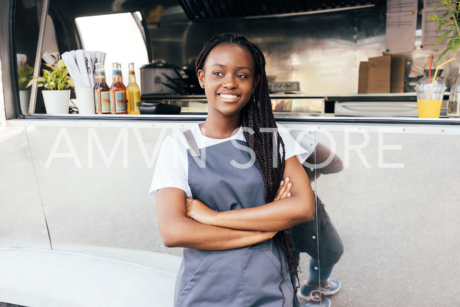 Smiling female entrepreneur wearing apron standing at a food truck. Saleswoman with arms crossed looking away.