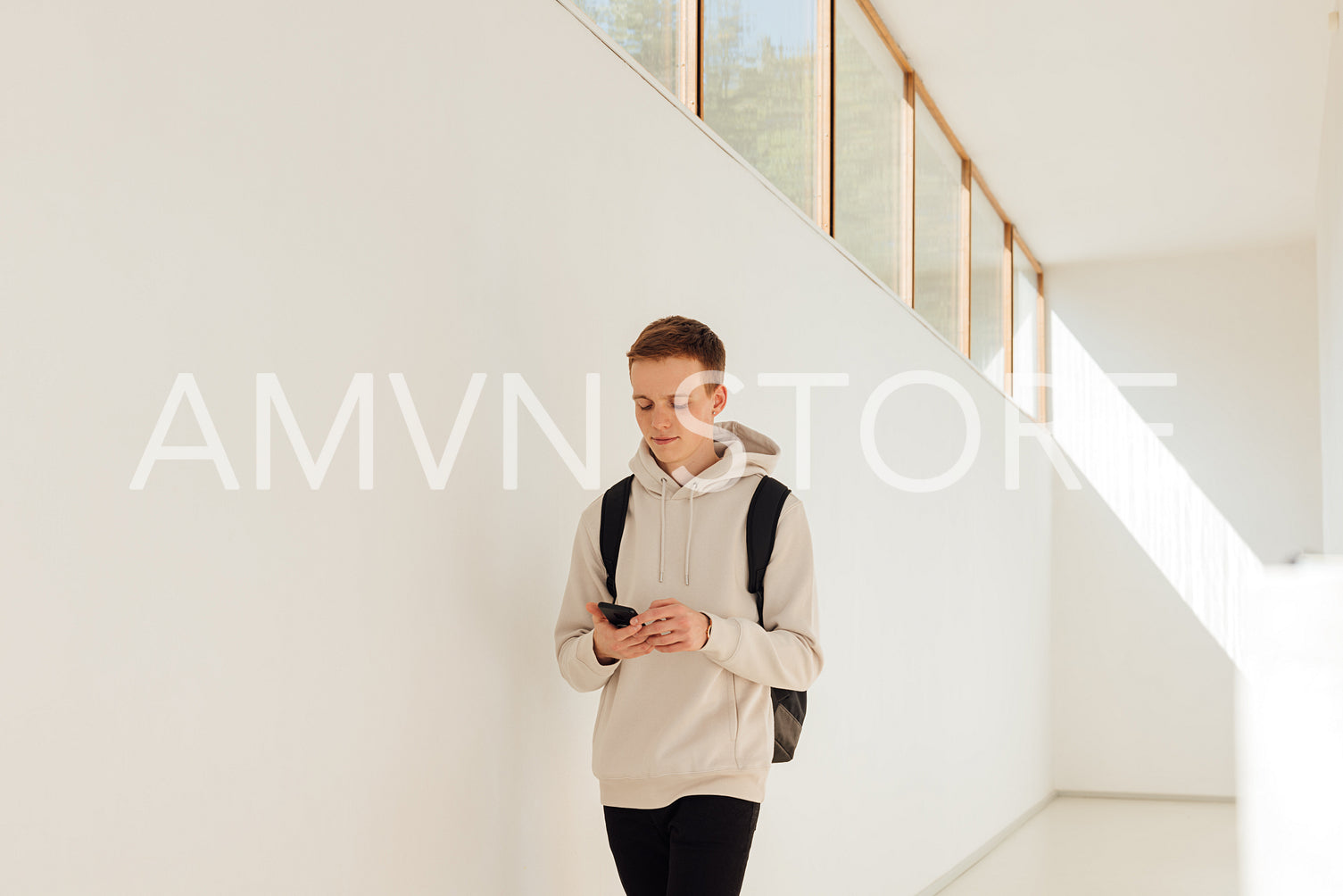 Male student walking in university corridor. Young man with smartphone in college.