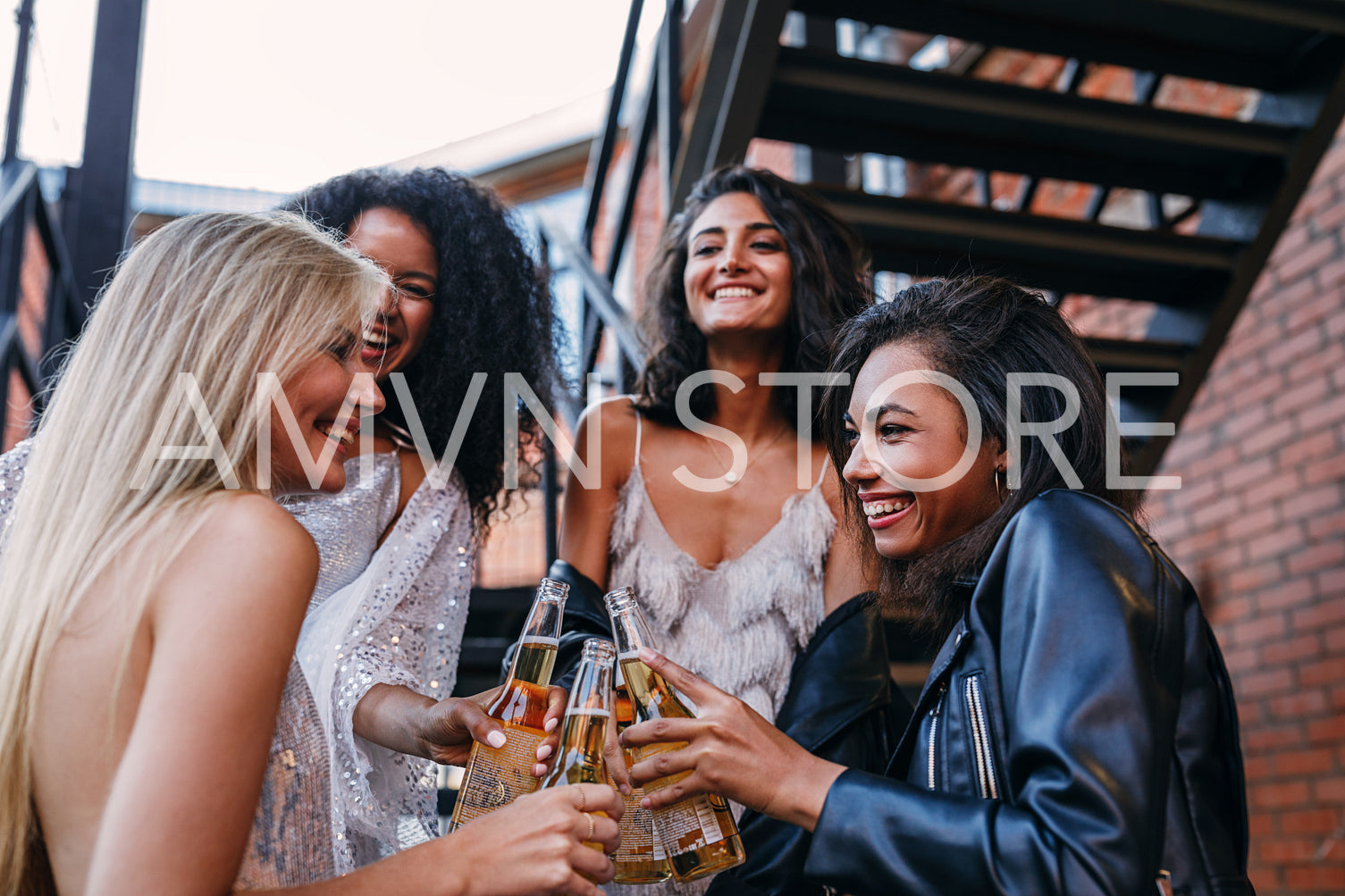 Beautiful laughing friends toasting with bottles of beer outdoors	