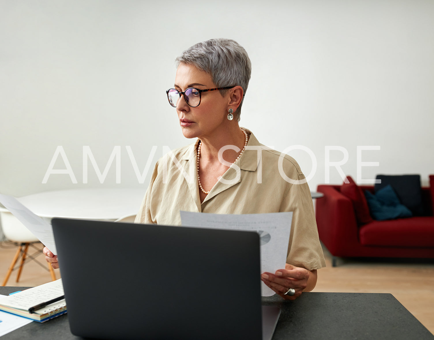 Mature woman sitting at a desk in a living room holding documents