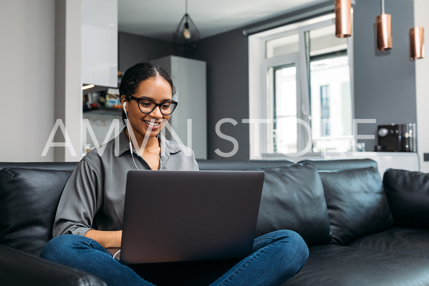 Young woman video calling using a laptop sitting on a sofa wearing earphones	