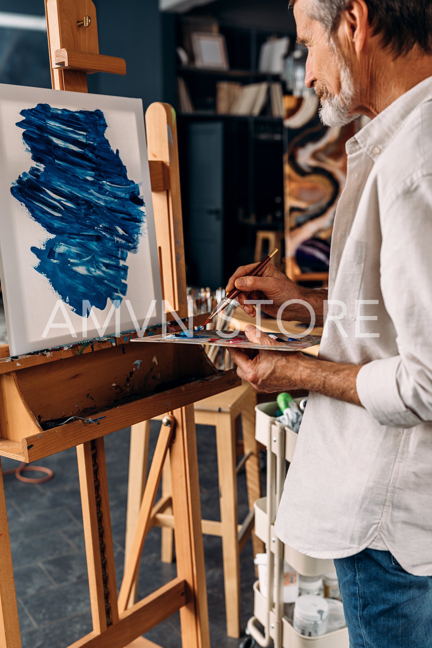 Senior painter standing in front of easel holding a paintbrush and palette	